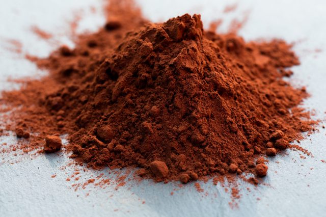 Pile of reddish-brown powder rests on a smooth, light-gray surface, scattered around with soft shadows.