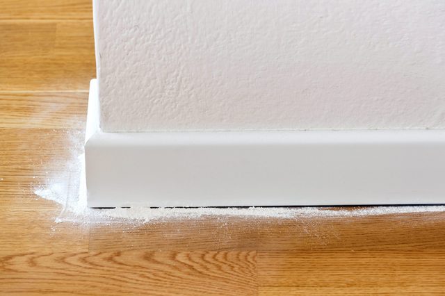 White powder rests against a white baseboard, adjacent to a wooden floor in a home interior setting.