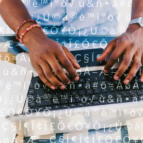 Hands typing on a laptop keyboard, overlayed with various accented letters and symbols, with a notebook and pen beside it on a desk.