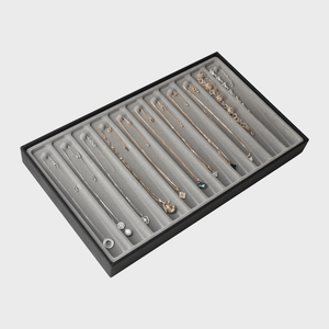 Necklaces displayed in organized rows within a black-bordered gray jewelry tray, showcasing various designs and pendants in a minimalist setting.