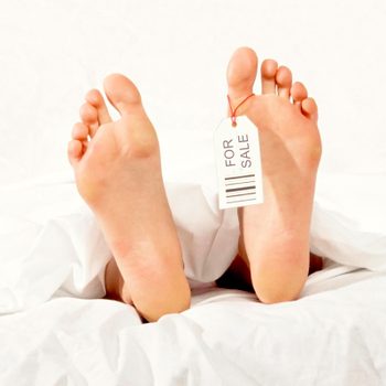 Feet lie still under white sheets, tagged "FOR SALE" on one toe, suggesting a humorous or morbid context.