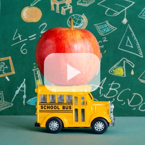 Toy school bus supports a red apple against chalkboard with educational drawings and equations.