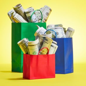 Bags hold rolled dollar bills, arranged in a group. The green, red, and blue bags contrast against a bright yellow background.