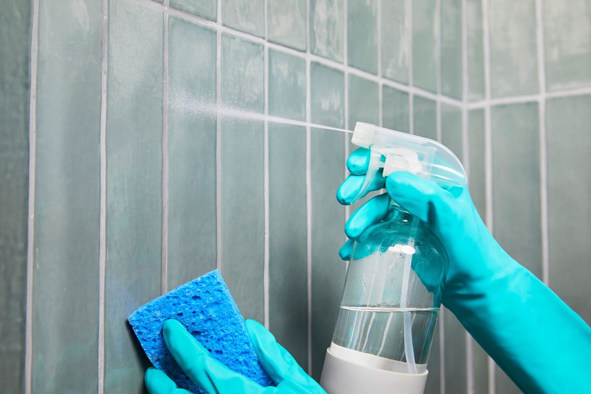 gloved hands spraying grout on a shower wall