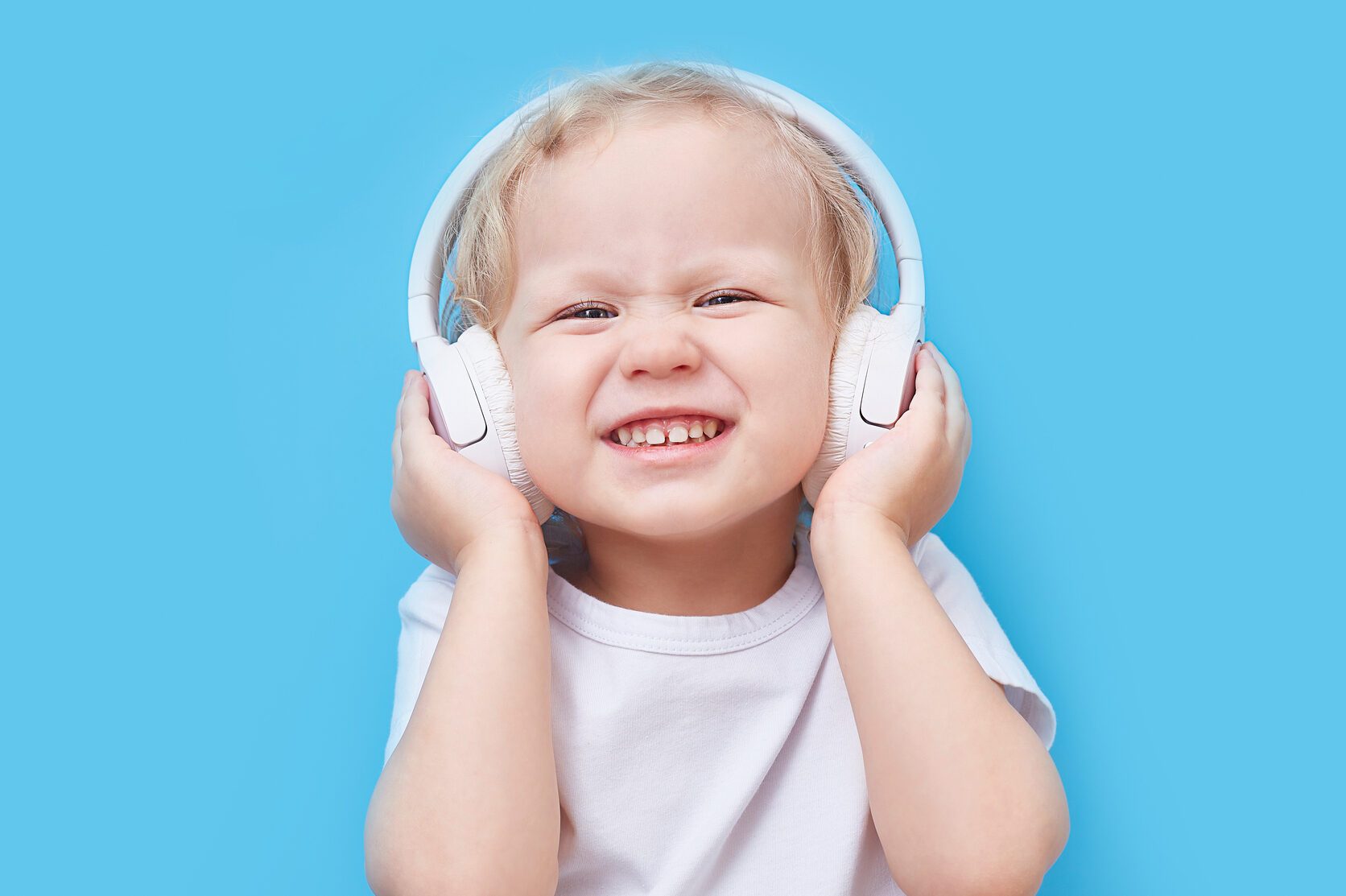 Child wearing headphones and a white T-shirt listens to music on a