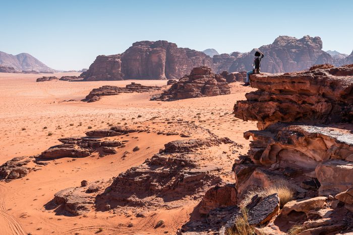 A woman traveller sitting on rock and looking to landscape of Wadi Rum desert in Jordan, Arab