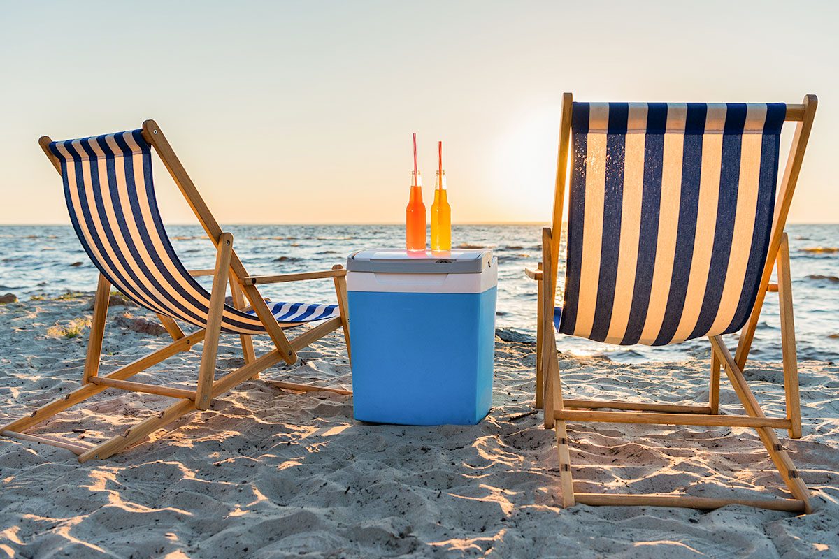 Refreshing beverages on cooler and chaise lounges on sandy beach at sunset
