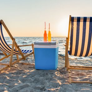 Refreshing beverages on cooler and chaise lounges on sandy beach at sunset