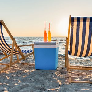 Refreshing beverages on cooler and chaise lounges on sandy beach at sunset