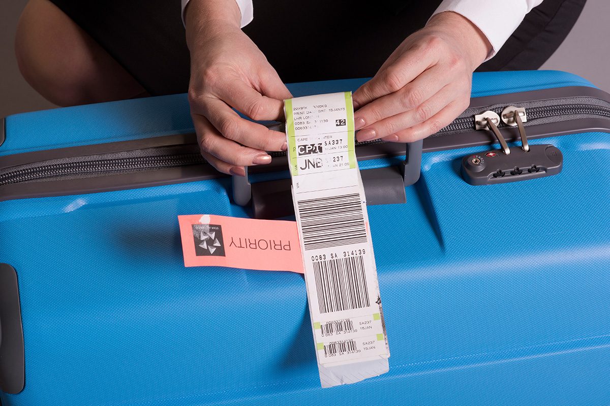Airline check in luggage tag being attached to a suitcase. Priority tags